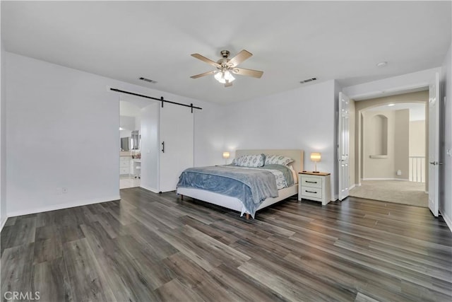 bedroom featuring a ceiling fan, a barn door, visible vents, and wood finished floors