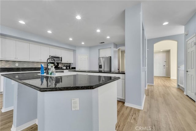 kitchen featuring light wood-type flooring, a center island with sink, arched walkways, and stainless steel appliances