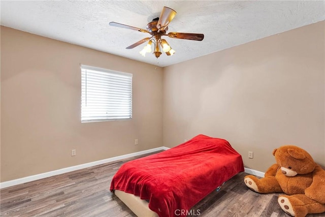 bedroom featuring ceiling fan, a textured ceiling, baseboards, and wood finished floors