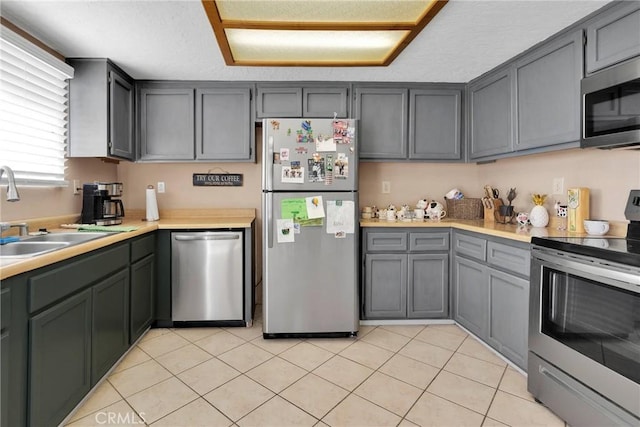 kitchen featuring light tile patterned floors, appliances with stainless steel finishes, light countertops, gray cabinetry, and a sink