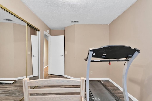 exercise room featuring a textured ceiling, baseboards, and wood finished floors