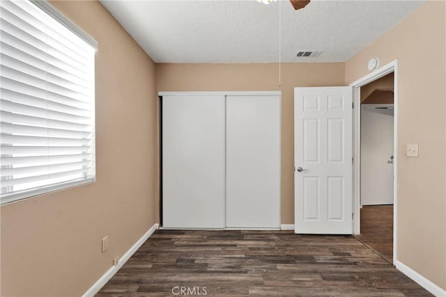 unfurnished bedroom with dark wood-style floors, a closet, visible vents, and baseboards