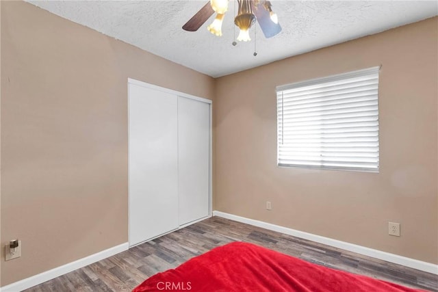 unfurnished bedroom featuring a closet, ceiling fan, a textured ceiling, wood finished floors, and baseboards