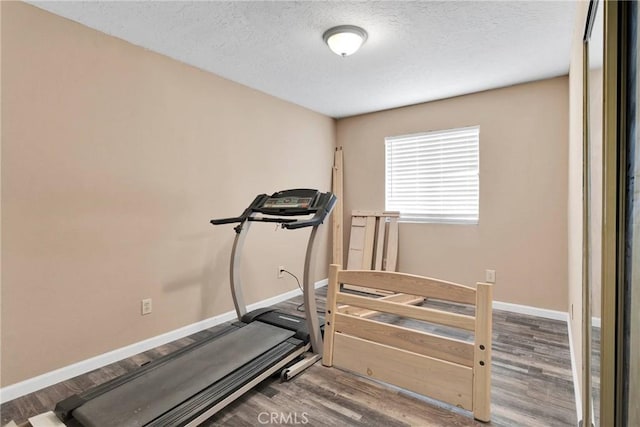 workout room featuring a textured ceiling, baseboards, and wood finished floors