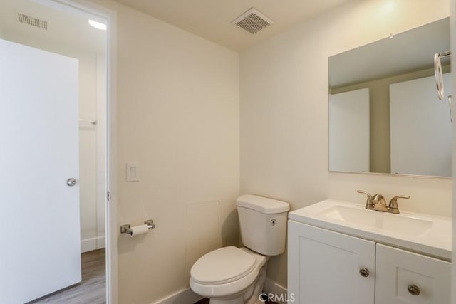 bathroom with toilet, vanity, visible vents, and baseboards