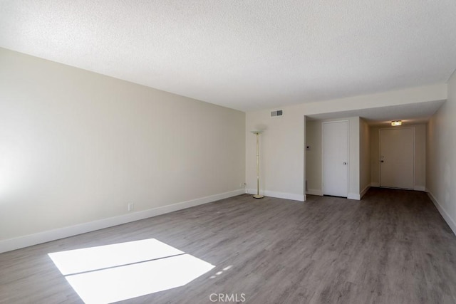 spare room with visible vents, baseboards, a textured ceiling, and wood finished floors