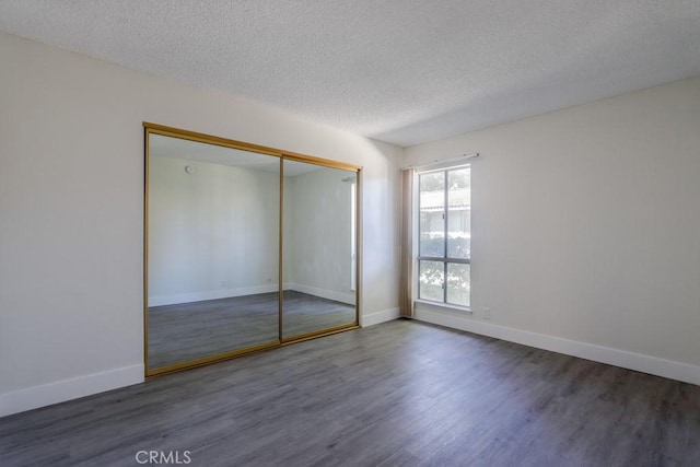 unfurnished bedroom featuring dark wood-type flooring, a textured ceiling, and baseboards