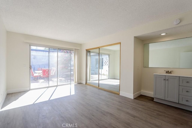 interior space with a textured ceiling, wood finished floors, a sink, and baseboards