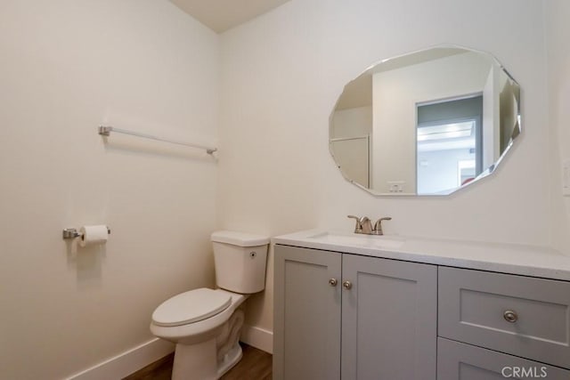 half bath featuring toilet, baseboards, wood finished floors, and vanity