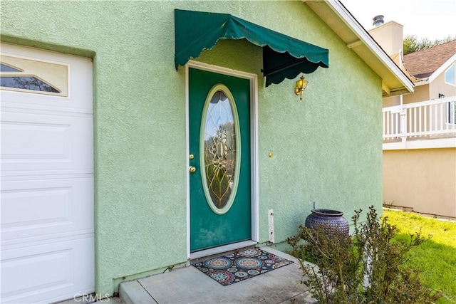 view of exterior entry with an attached garage and stucco siding