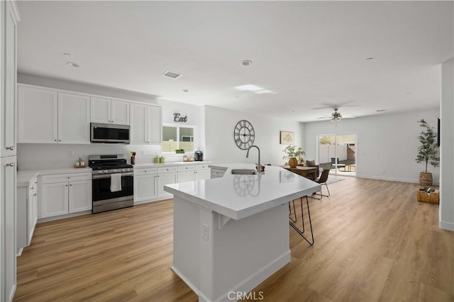 kitchen featuring a center island with sink, visible vents, stainless steel appliances, white cabinetry, and a sink