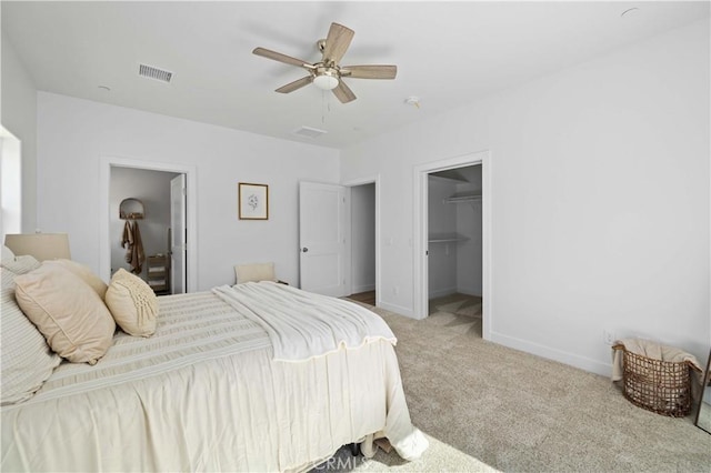 bedroom featuring ceiling fan, light colored carpet, visible vents, baseboards, and a walk in closet