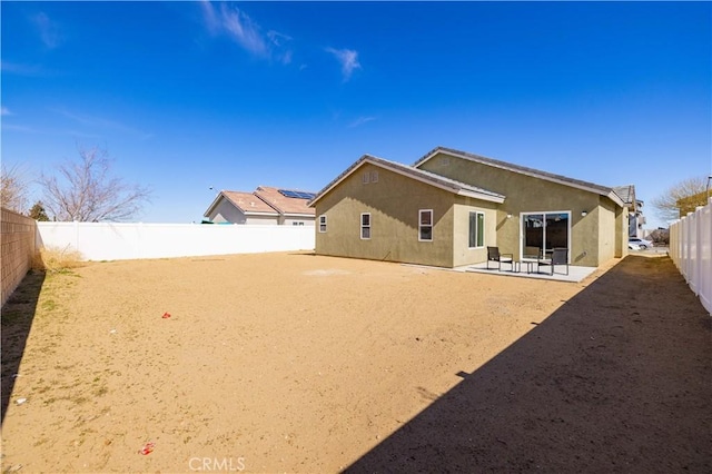 back of house featuring a fenced backyard, dirt driveway, a patio, and stucco siding