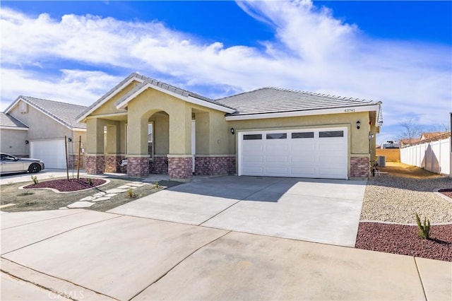 view of front of property featuring stucco siding, fence, a garage, stone siding, and driveway