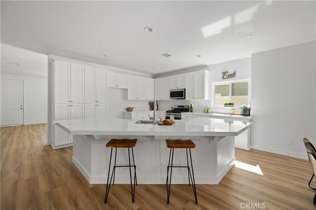 kitchen featuring a kitchen island with sink, appliances with stainless steel finishes, white cabinets, and light countertops