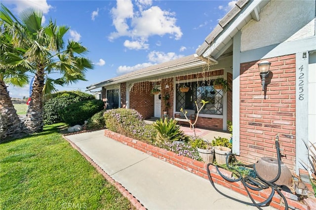 entrance to property featuring brick siding and a yard