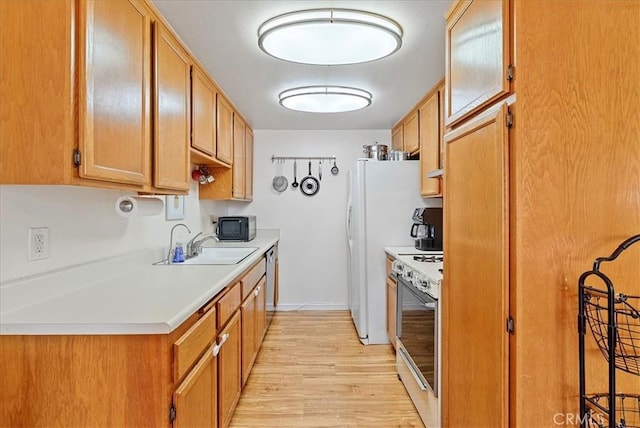 kitchen featuring black microwave, a sink, white range oven, light countertops, and light wood finished floors