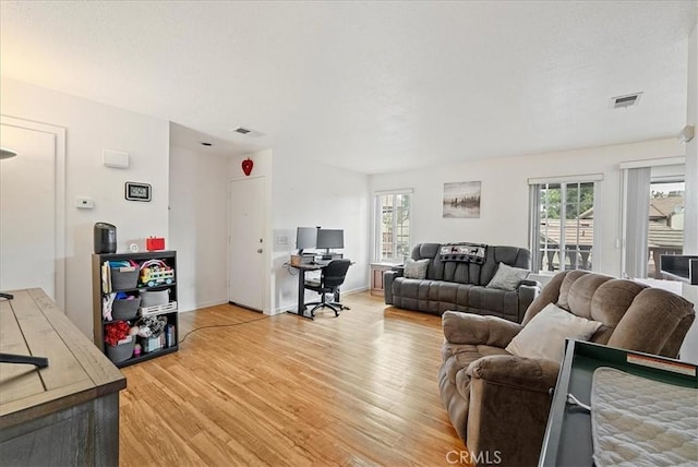 living room featuring light wood-type flooring, visible vents, and a wealth of natural light