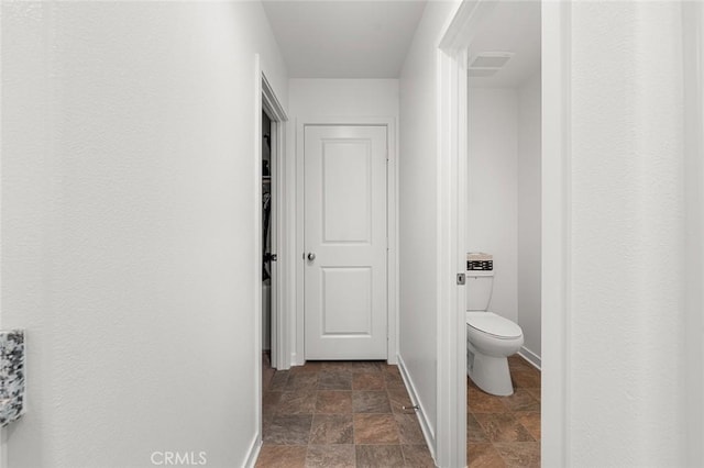 bathroom featuring toilet, stone finish floor, and baseboards