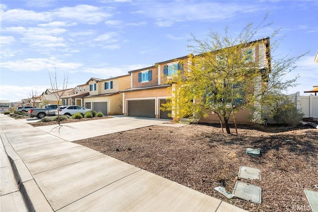 view of front facade with a garage, concrete driveway, a residential view, fence, and stucco siding