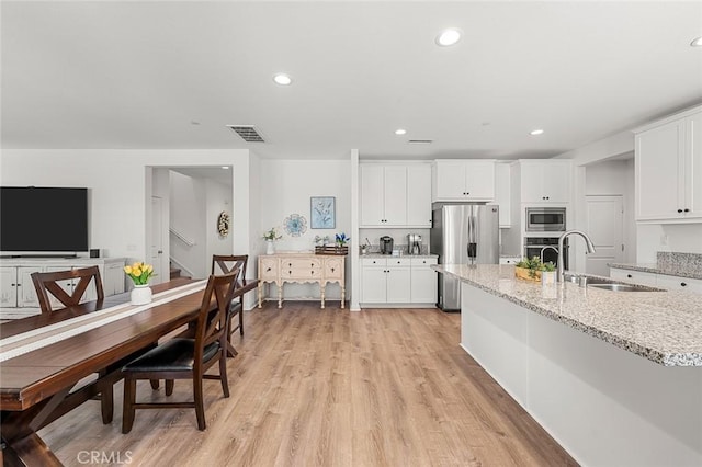 kitchen featuring visible vents, white cabinets, light stone countertops, stainless steel appliances, and a sink