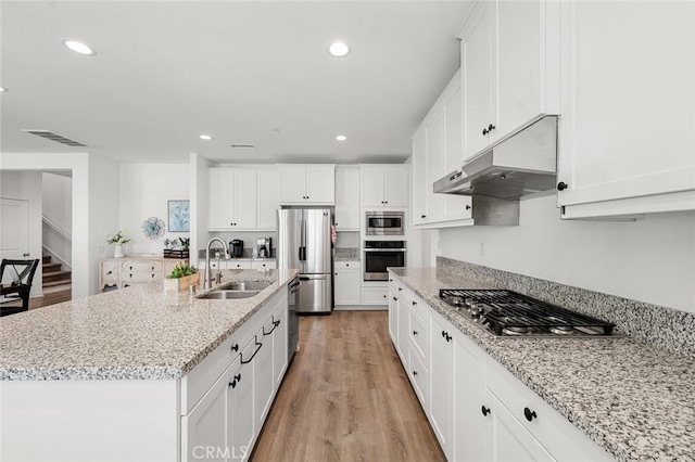 kitchen with under cabinet range hood, a sink, white cabinets, appliances with stainless steel finishes, and a center island with sink