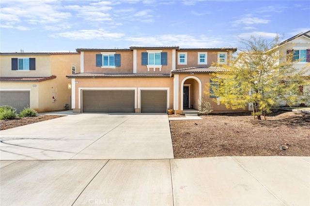 mediterranean / spanish home with a garage, driveway, a tiled roof, and stucco siding