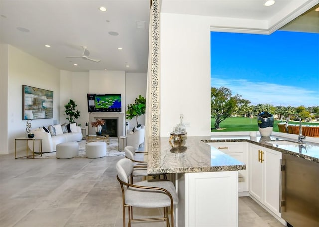 75851 Via Pisa, Indian Wells, CA 92210 - kitchen featuring light stone counters, a breakfast bar area, white cabinetry, open floor plan, and a glass covered fireplace