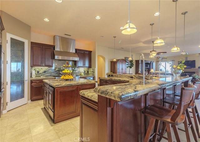 kitchen featuring wall chimney range hood, arched walkways, a spacious island, and decorative backsplash