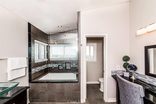 bathroom with toilet, vanity, wood finished floors, baseboards, and a bath