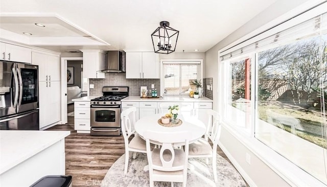 kitchen with wall chimney range hood, white cabinetry, appliances with stainless steel finishes, and light countertops