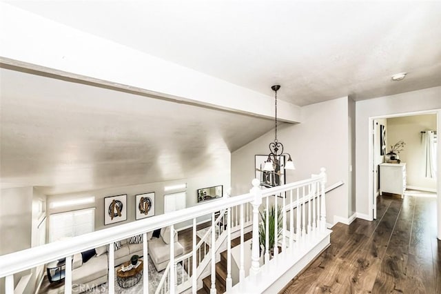 corridor featuring baseboards, dark wood-type flooring, an upstairs landing, and a notable chandelier