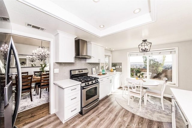 kitchen with light countertops, wall chimney range hood, stainless steel gas range oven, and white cabinetry