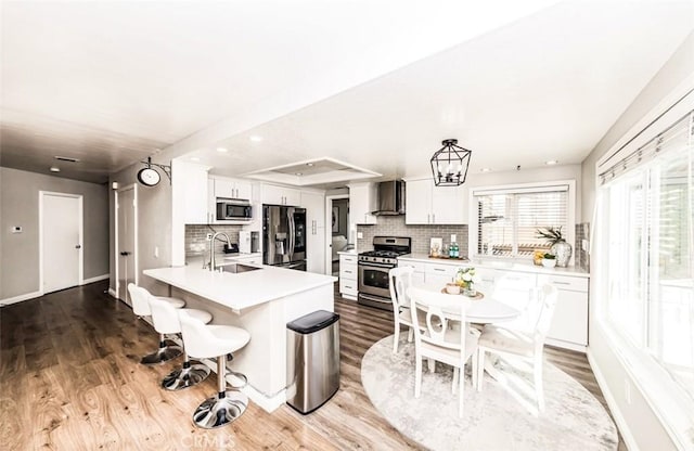 kitchen featuring stainless steel appliances, light countertops, white cabinets, a sink, and wall chimney range hood