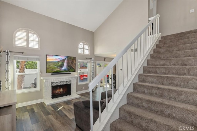 stairs featuring a fireplace, high vaulted ceiling, a wealth of natural light, and wood finished floors