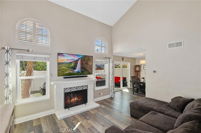 living area featuring a wealth of natural light, a brick fireplace, wood finished floors, and visible vents