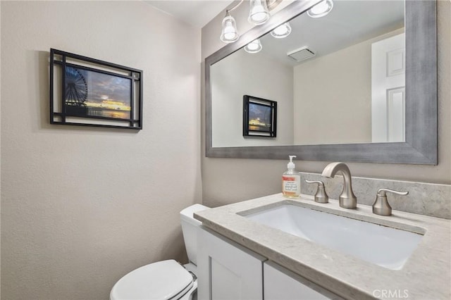 half bathroom featuring visible vents, vanity, and toilet