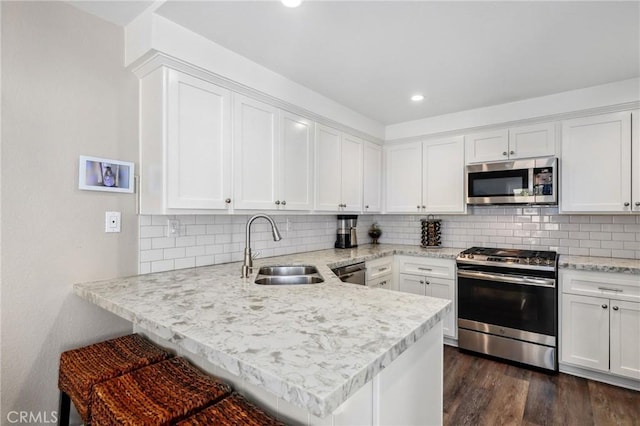 kitchen with stainless steel appliances, a peninsula, a sink, and white cabinets