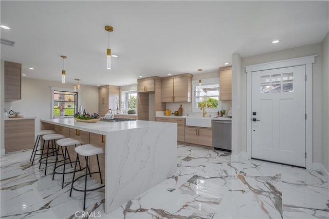 kitchen featuring a center island with sink, modern cabinets, appliances with stainless steel finishes, decorative light fixtures, and light brown cabinets