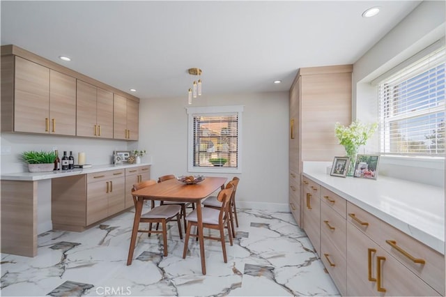 kitchen featuring marble finish floor, light countertops, hanging light fixtures, light brown cabinetry, and modern cabinets