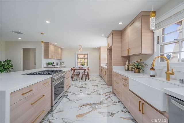 kitchen with appliances with stainless steel finishes, light countertops, light brown cabinetry, pendant lighting, and a sink