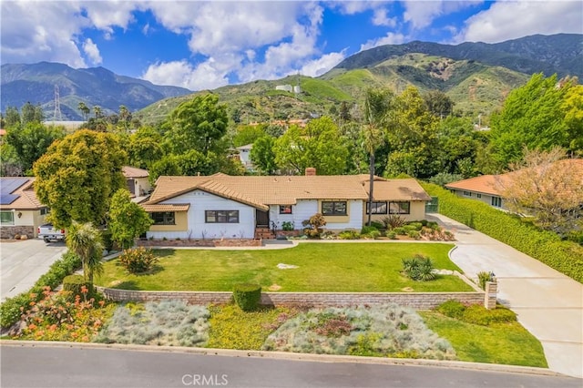 exterior space with a mountain view, a tile roof, driveway, a chimney, and a front yard