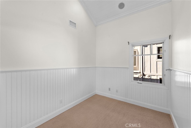 carpeted empty room with visible vents, wainscoting, lofted ceiling, and ornamental molding