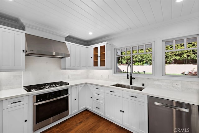 kitchen featuring backsplash, crown molding, appliances with stainless steel finishes, wall chimney exhaust hood, and a sink