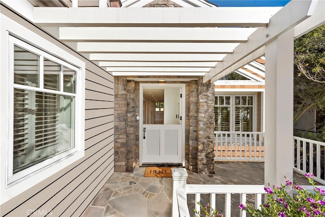 entrance to property with stone siding, covered porch, and a pergola