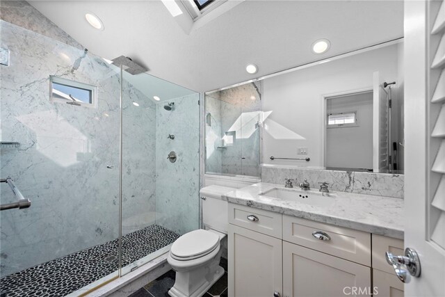 bathroom with a marble finish shower, toilet, a skylight, and vanity