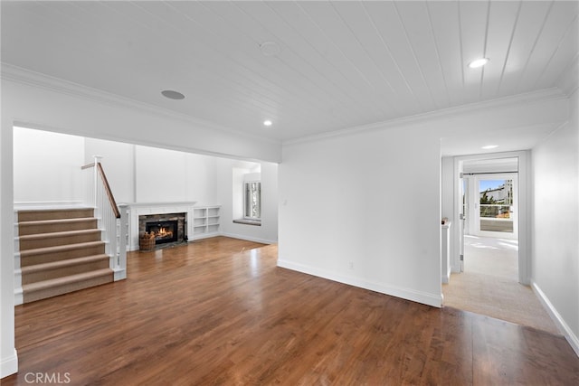 unfurnished living room with ornamental molding, a warm lit fireplace, wood finished floors, baseboards, and stairs