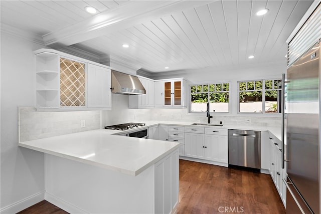 kitchen featuring a peninsula, open shelves, a sink, appliances with stainless steel finishes, and wall chimney exhaust hood