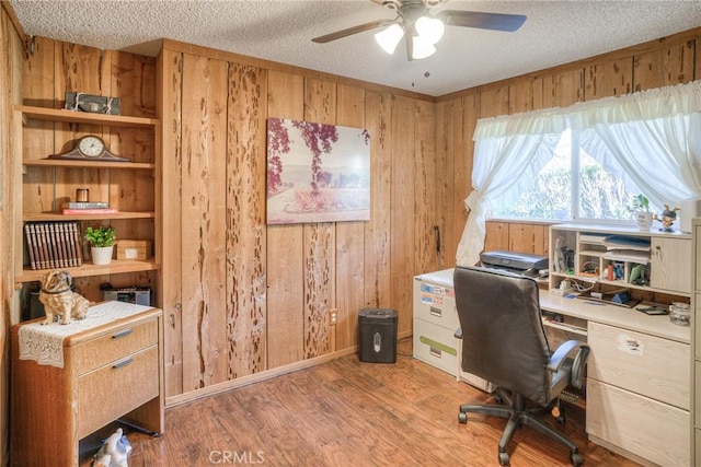 office area with a textured ceiling, wood walls, and light wood-type flooring