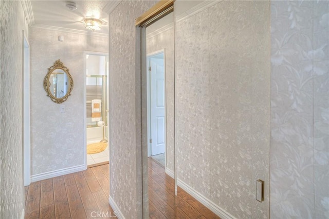 hallway with wallpapered walls, baseboards, ornamental molding, and wood finished floors
